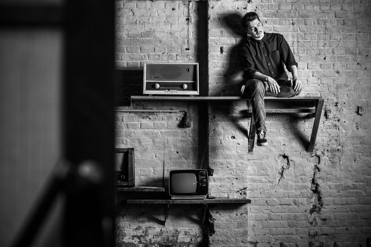 Joscha David Moret sitzt auf einem Wandregal neben einem Retro-Radio vor einer Ziegelwand im Schärferaum